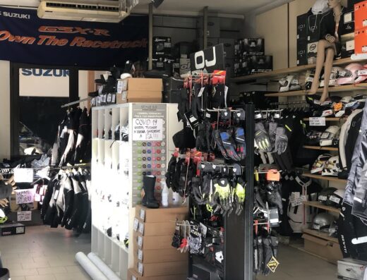 Interno del negozio Duilio Moto, concessionaria Suzuki, con esposizione di abbigliamento tecnico, caschi, guanti e accessori per motociclisti.