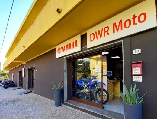 Esterno del negozio DWR Moto, rivenditore Yamaha, con una moto blu in esposizione dietro la vetrina. Servizi di vendita, accessori e assistenza moto.