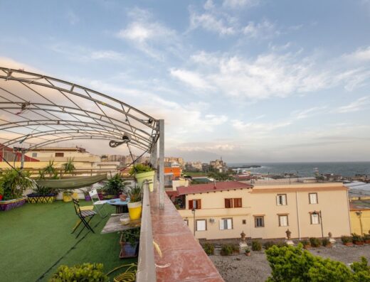 Terrazza panoramica dell'Eco Hostel Floreale con vista sul mare, arredi colorati, piante e struttura ombreggiante in metallo.