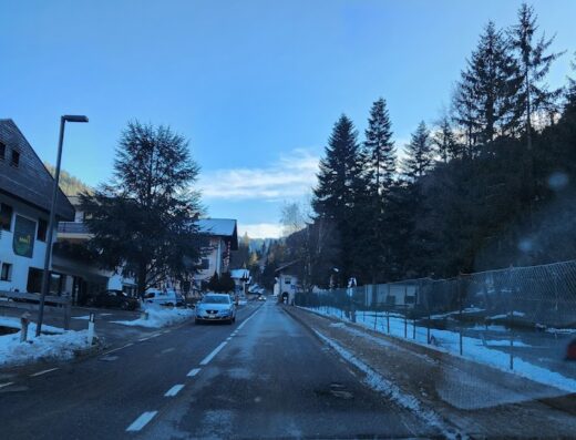 Strada di montagna innevata con case e auto, ideale per viaggi in moto e scooter offerti da Eco System Motors s.r.l.s.