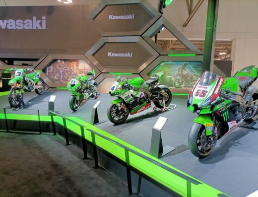 Esposizione di moto Kawasaki a EICMA, con modelli da cross, da corsa e sportive in verde e nero, presentate su una piattaforma illuminata.