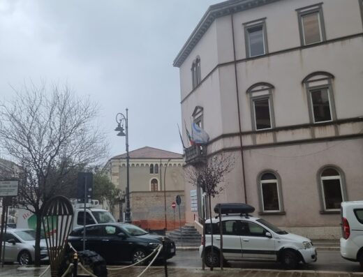 Elettrauto a Isernia: Vista di un monumento con paracadute e pneumatico, auto parcheggiate e architettura locale in una giornata nuvolosa.