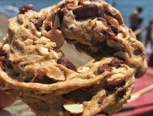 Tarallo pugliese artigianale con mandorle, tipico snack da forno della Puglia, sullo sfondo spiaggia e mare. Prodotto da forno tradizionale italiano.