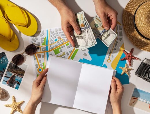 Preparations for a tour: Hands counting U.S. dollars on a map, surrounded by a notebook, camera, hat, sunglasses, beach photos, flip-flops and starfish, suggesting travel planning.