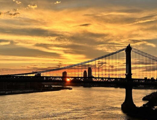 Ponte di Brooklyn al tramonto, con cielo arancione e nuvole drammatiche, vista panoramica sul fiume.
