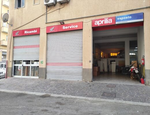 Esposto Moto S.R.L.: Facciata del negozio con insegne Honda Ricambi, Service e Aprilia concessionaria, moto parcheggiata all'interno.