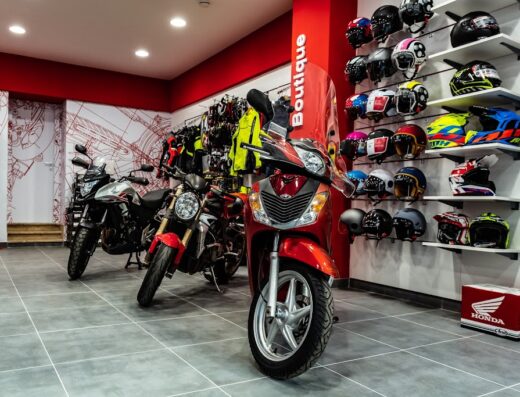 Esposizione di moto nuove e accessori nel negozio Espressionemoto S.r.l.: scooter rosso Honda in primo piano, moto e caschi da motociclista sullo sfondo. Ampia scelta di veicoli e abbigliamento per motociclisti.