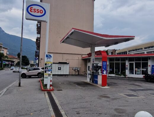 Stazione di servizio Esso a Lecco con insegna ben visibile, pompe di benzina con tettoia rossa e bianca, prezzi del carburante esposti. Ideale per motociclisti in viaggio che necessitano di rifornimento.