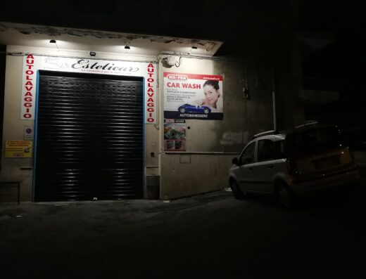 Esteticar car wash service with closed shutter at night; an advertisement for MA-FRA Car Wash is visible, promoting car care and autobenessere services.