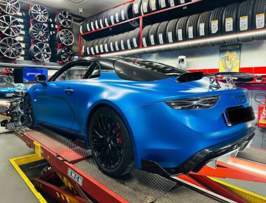 Eurogomme: Blue Alpine sports car on a lift in a tire shop, with tire racks and wheel displays visible in the background.