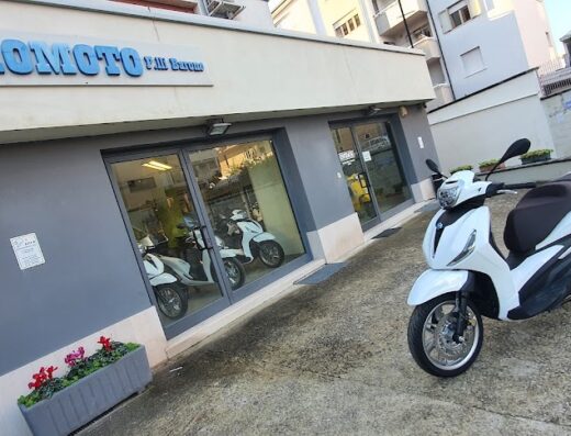 Scooter bianco parcheggiato di fronte al negozio Euromoto, concessionario di moto e accessori per motociclisti, con vetrine che mostrano altri scooter.