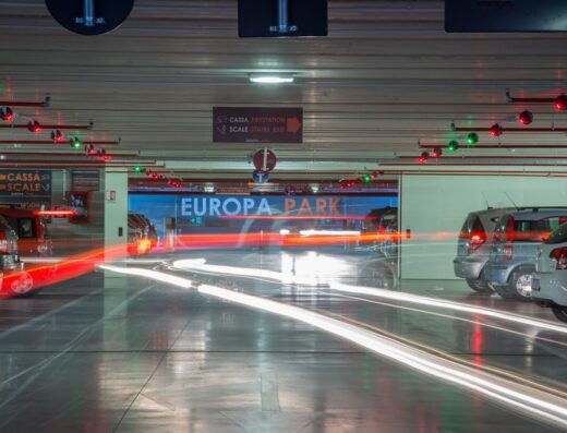 Illuminated underground parking garage at Europa Park with cars, exit signs, and motion blur from vehicle lights.