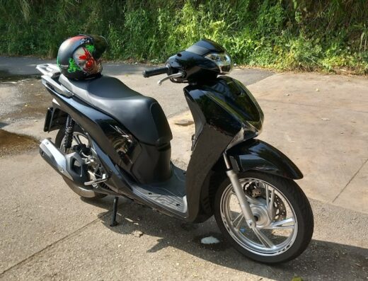 F.G. Autolavaggio: Scooter nero Honda SH parcheggiato all'aperto con casco decorato appoggiato sulla sella, ideale per il lavaggio moto.
