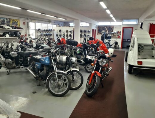 Esposizione di moto d'epoca e accessori in un negozio. Diverse moto e scooter visibili, inclusa una Citroen smontata. Caschi esposti sullo sfondo.
