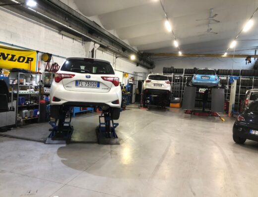 Interno di un'officina meccanica con auto sollevate su piattaforme per la riparazione e manutenzione, e pneumatici impilati sullo sfondo