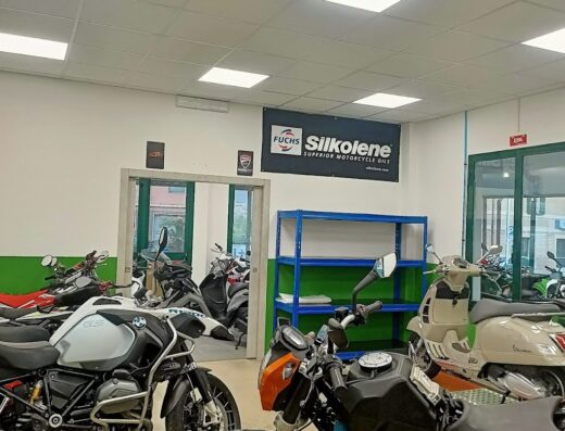 Officina Falcone Moto: diverse motociclette e scooter in riparazione, tra cui BMW GS e KTM Duke, con scaffalature e cartello Silkolene.