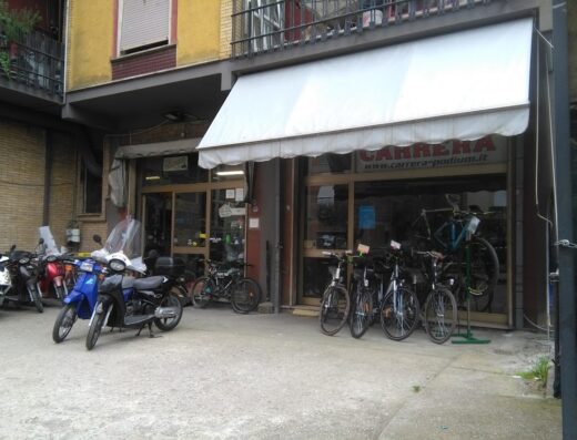 Negozio Carrera con vetrina di biciclette e scooter parcheggiati di fronte, vendita e accessori per ciclisti a Falocco Alvaro.