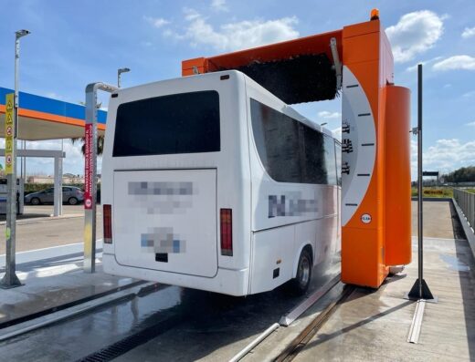 Autobus bianco in un autolavaggio automatico arancione, con spazzole rotanti. L'autobus sta ricevendo un lavaggio rapido.