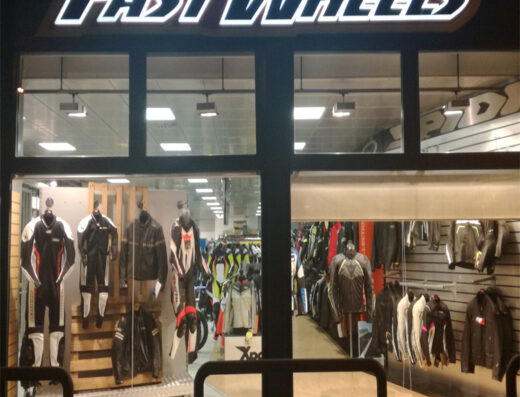 Vetrine del negozio Fast Wheels con abbigliamento e accessori per motociclisti, tute in pelle, giacche e caschi in esposizione.