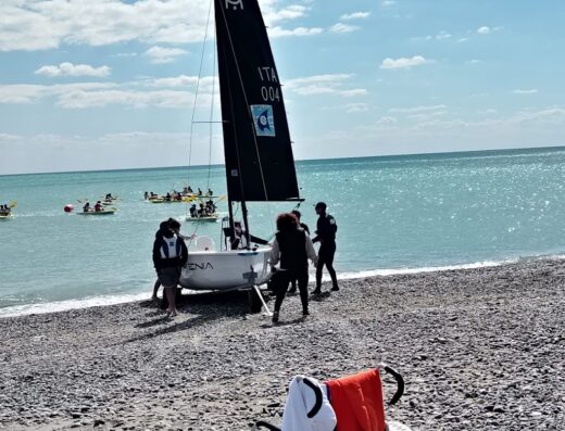 Sedia a rotelle sulla spiaggia con barca a vela e persone in acqua. Vacanza accessibile e viaggi inclusivi con Fc Viaggi S.r.l.s.