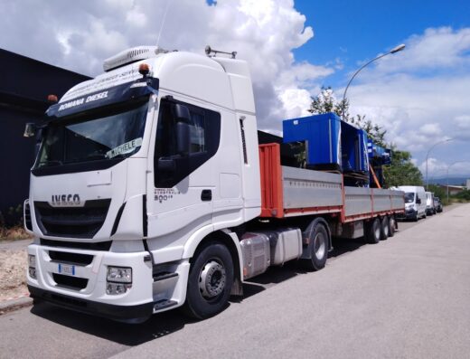 Camion Iveco bianco di Romana Diesel Ecocentralia 500 con rimorchio che trasporta una struttura blu per ReNova Washtec di Feland S.a.s.