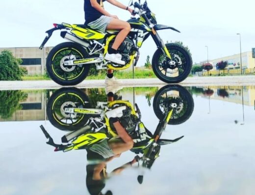 Ragazzo con casco su moto Ferali Moto gialla e nera, riflessa in una pozzanghera. Ideale per esplorare nuovi percorsi e avventure.