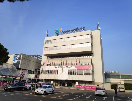 Esterno di Fiera Verona, con bandiere, insegna "Veronafiere" e parcheggio antistante. Eventi, servizi e marketplace per il settore moto.