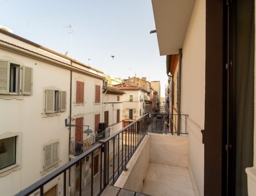 Vista dal balcone di FLOW room&breakfast su una tipica strada italiana con edifici storici e persiane colorate.