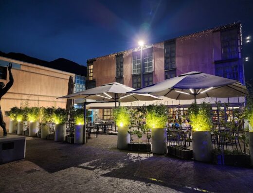 Esterno serale illuminato di un hotel Fly Bike con tavoli e ombrelloni, ideale per motociclisti in viaggio e per servizi turistici