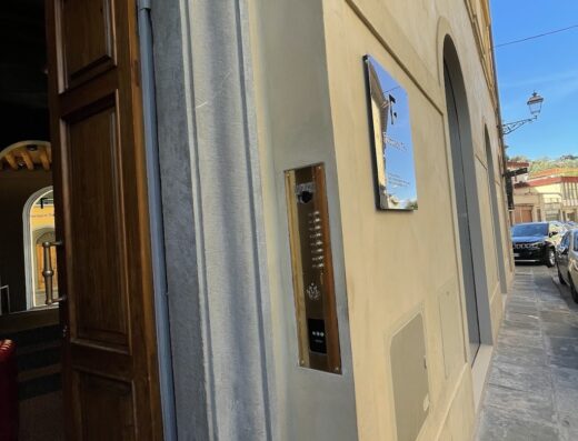 Ingresso della Fornace Suite, con porta in legno aperta e citofono in ottone a parete. Dettaglio dell'architettura esterna.