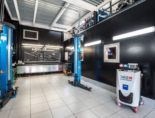 Interno di un'officina meccanica con due sollevatori per auto, banco da lavoro con utensili Alfa Romeo e macchina per la ricarica del gas refrigerante. Servizi di riparazione e manutenzione moto.