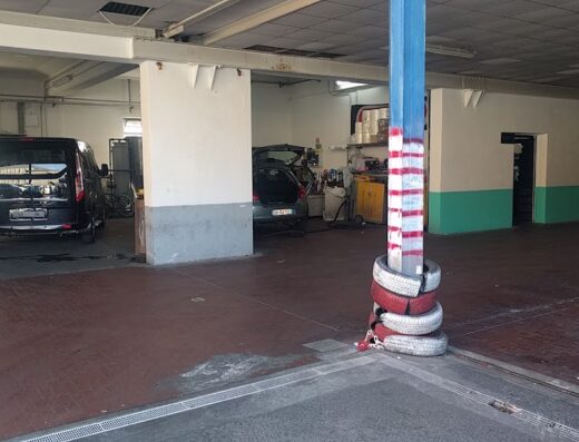 Interno dell'officina Fratelli Ierace Sas, con auto in riparazione, pneumatici impilati e attrezzature per il servizio gomme e autolavaggio.