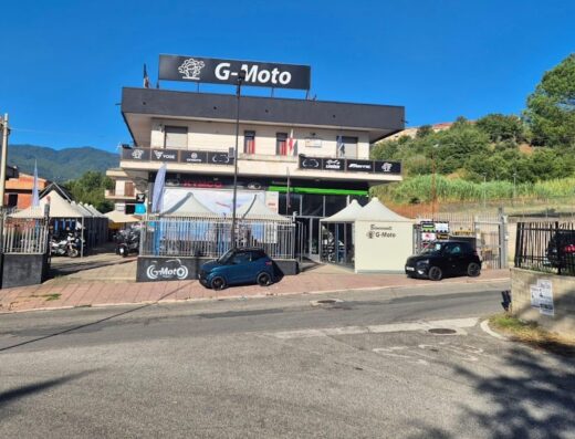 G-Moto negozio di moto e accessori a Scalea, Calabria. Vetrina di concessionario con marchi Kymco, Beta e altri. Auto parcheggiate di fronte all'ingresso.