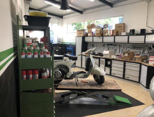 G.P. Motors di Giacomo Pizii: Officina specializzata in riparazione e restauro di moto e scooter Vespa d'epoca. Visuale di una Vespa bianca su un ponte sollevatore, scaffale con prodotti Wurth, banco da lavoro con attrezzi.