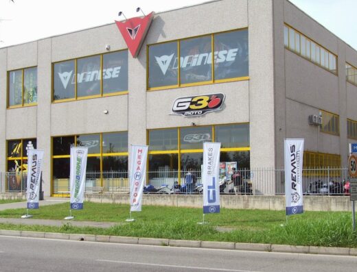 Foto dell'esterno del negozio di moto G3 Moto con insegne Dainese, cartelli Mega Motor, Remus, e moto visibili all'interno. Servizi e accessori per motociclisti.