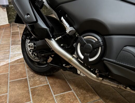 Dettaglio di una motocicletta nera con scarico aftermarket in acciaio. Accessori e modifiche per moto, vendita e riparazione.