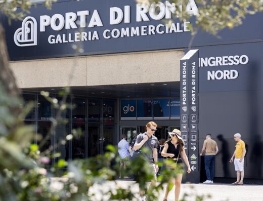 Ingresso principale della Galleria Commerciale Porta di Roma con persone che entrano e cartelli segnaletici visibili.