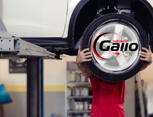 Un meccanico al lavoro su un'auto sollevata con il logo di Pneumatici Gallo sovrapposto alla ruota. Servizi di riparazione e manutenzione auto.