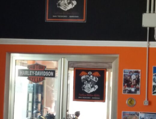 Gallura Custom Cycles SRL: View of the interior showing custom motorcycle builds, Harley-Davidson sign, and vintage motorcycle posters in San Teodoro, Sardinia.