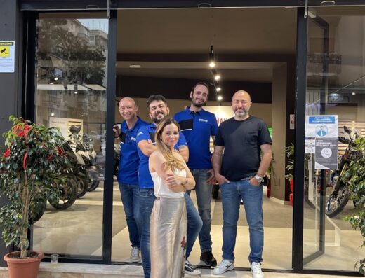 Un gruppo di persone posa davanti a Gambino Moto Yamaha, concessionaria di moto, abbigliamento e accessori per motociclisti