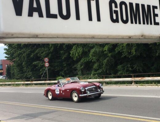Auto d'epoca rossa targata "642 SPG" guidata su strada asfaltata sotto l'insegna "VALOTTI GOMME", Garage 776 officina gommista