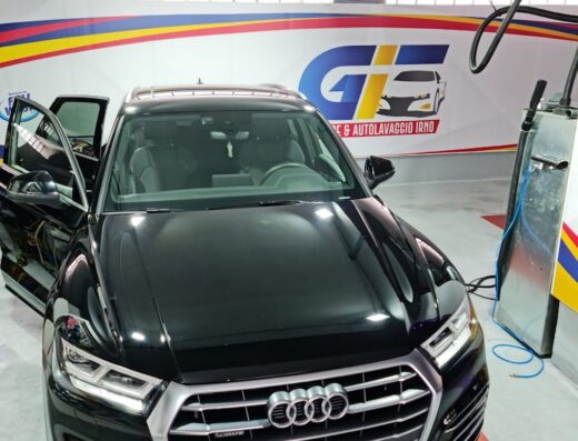 Autovettura Audi nera in un autolavaggio, con lo sportello aperto e l'insegna "Garage & Autolavaggio IRNO" sullo sfondo.