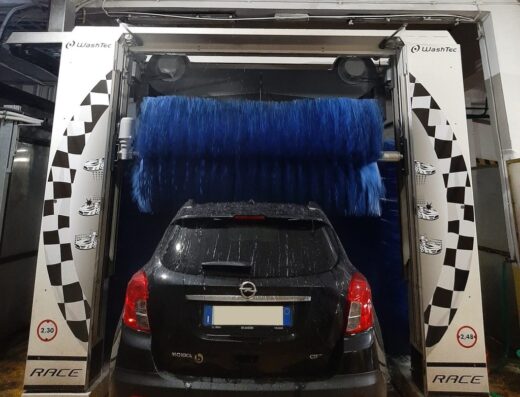 Autolavaggio Palace: Opel Mokka nera in un impianto di autolavaggio automatico WashTec con spazzole blu rotanti e decorazioni a scacchi.