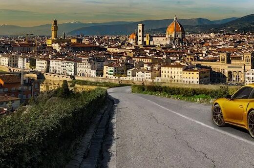 Garage Firenze Centro: Vista panoramica di Firenze con una Porsche dorata in primo piano. Servizi di garage, parcheggio custodito e accessori moto disponibili.