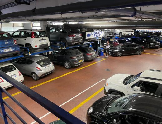 Garage La Stazione Firenze: interno del parcheggio multipiano con auto disposte su piattaforme e indicazioni 'Uscita'.