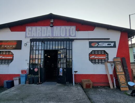 GardaMoto negozio di abbigliamento e accessori moto: facciata esterna con insegna, vetrine con loghi Alpinestars e Sidi, e moto parcheggiata. Vendita e assistenza per motociclisti.