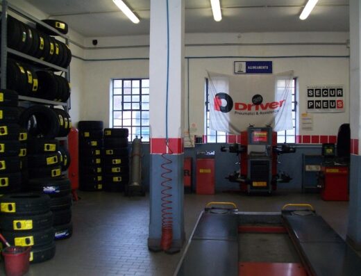 Interno dell'officina Driver Center Pirelli a Genova, con scaffali di pneumatici, banco di lavoro per l'allineamento ruote e attrezzature per la manutenzione moto.