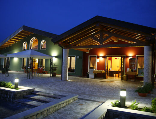 Gelindo dei Magredi: esterni illuminati di sera, architettura tipica con portico in legno, ristorante accogliente per motociclisti in viaggio.