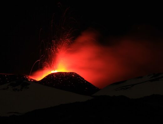 Eruzione notturna dell'Etna durante un tour guidato. Il vulcano attivo sputa lava incandescente e fumo rosso, creando uno spettacolo suggestivo. Escursioni e avventure in moto sull'Etna con Geo Etna Explorer.