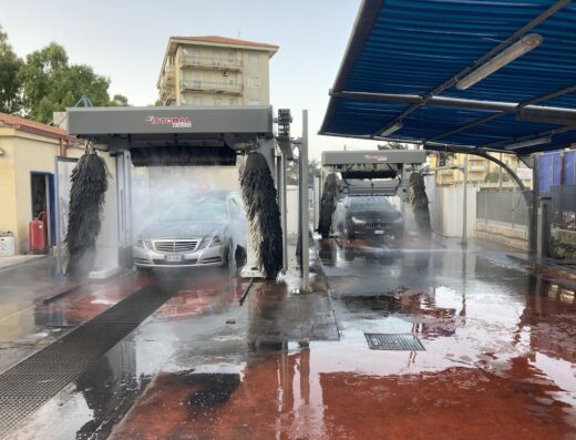 Autolavaggio GF: due auto in fase di lavaggio automatico con spazzole rotanti e getti d'acqua, servizio di pulizia auto professionale.